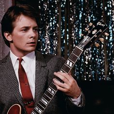 a man in a suit and tie holding an electric guitar while wearing a red tie