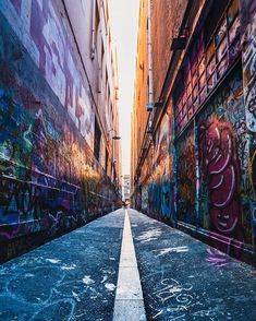 an alleyway with graffiti on the walls and concrete pavement in between two large buildings