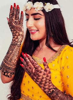 a woman wearing henna and holding her hands up to the side with flowers in her hair