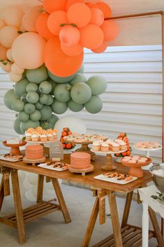 a table topped with cakes and cupcakes next to a bunch of balloons hanging from the ceiling