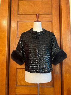 "Flashy & classy short sleeved black sequined jacket from the 1960s with fur cuffs. Looks great as a layer over a fancy look or instantly dresses up a more casual outfit. The fur is real, as far as I can tell. This piece has a one-snap closure with a faux sequined button, a thicker collar, and hangs freely. Best for a M based on the shoulder measurement, but could work for an S or L. It's lined with black satin and it feels like there's a light layer of insulation between the sequins and the sat Winter Black Outerwear With Contrast Sequin, Vintage Festive Sequin Outerwear, Vintage Fitted Sequin Outerwear, Vintage Mink Outerwear With Faux Fur Trim, Luxury Vintage Mink-colored Outerwear, Satin Noir, Sequin Jacket, Black Satin, Look Chic