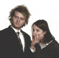 a man and woman standing next to each other in front of a white wall with their hands on their face