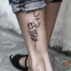 a woman's foot with a skull and flowers tattoo on the side of her leg