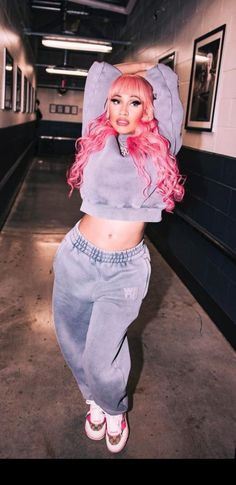 a woman with pink hair wearing grey sweatpants and a hoodie is posing for the camera