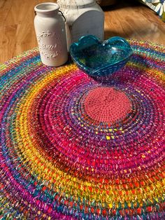 a multicolored round rug on the floor next to a jar and glass vase