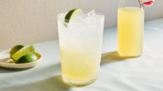 two glasses filled with lemonade and limes on a table