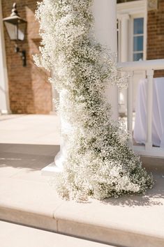 white flowers are growing up the side of a pillar in front of a brick building