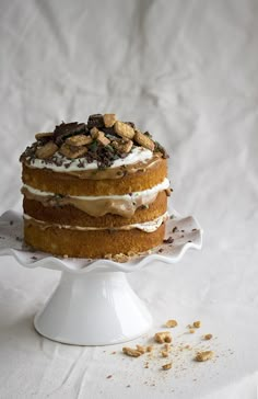 there is a cake with nuts on the top and frosting in the middle, sitting on a white pedestal