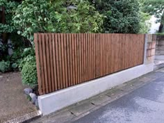 a wooden fence on the side of a road next to some bushes and trees in front of a house