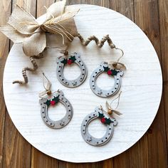 three metal horseshoes with christmas decorations hanging from them on a white plate next to a burlwood bow