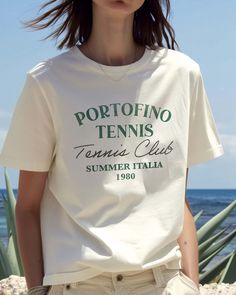 Grab your Vespa and your racket and get to the Portofino Tennis Club. Your retro passport to a stylish summer in Italia 1980. Ciao, bella! Unisex soft cotton crew neck t-shirt featuring a Portofino Tennis Club Italy 1980 graphic printed on the front. Fabrics: 100% cotton, 6.1 oz Made in: LA Models wearing S/M Italy Graphic, Portofino Italy, Graphic Tee Vintage, Tennis Club, Retro Sports, Retro Sport, Tennis Clubs, Ciao Bella, Vacation Travel