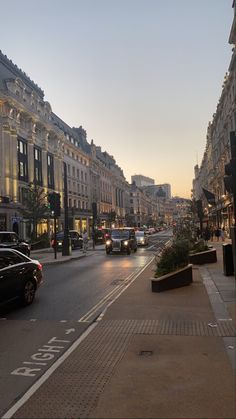 a city street filled with lots of traffic next to tall buildings and trees at dusk