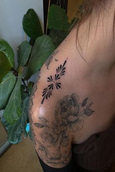 a woman's back with flowers on it and leaves around her shoulder, in front of a plant