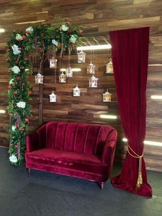 a red velvet couch and chair in front of a wooden wall decorated with hanging decorations