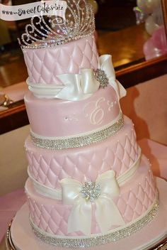 a three tiered pink wedding cake with white bows and a tiara on top