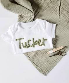 a white shirt with the word tucker written on it next to scissors and some fabric