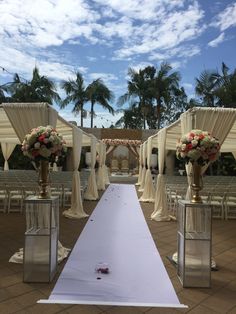 an outdoor wedding setup with white drapes and floral centerpieces on the aisle