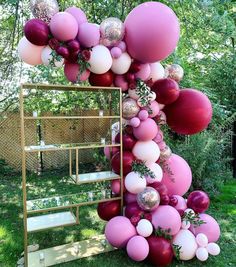 a bunch of balloons that are hanging from a pole in the grass near some trees