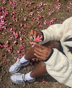 a woman sitting on the ground with pink flowers in her hands and one hand holding something