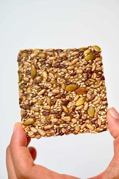 a person holding up a piece of granola bar with nuts and seeds on it