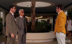 three men in suits and sunglasses are talking to each other while others walk past them