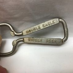 two metal bottle openers with the words double eagle and ginger beer on them are being held by someone's hand