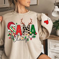 Mama Claus Christmas Sweatshirt – Personalized with Kids’ NamesGet into the festive spirit with our "Mama Claus" Christmas Sweatshirt! Featuring a cute design with a Santa hat atop the first "M" and reindeer horns on the second, this cozy sweatshirt is perfect for all the holiday-loving mamas. Twinkling Christmas lights line the bottom, and to make it extra special, you can personalize the left sleeve with up to 5 kids' names, each placed under a heart. Whether it's 1, 2, 3, 4, or 5 hearts, this Twinkling Christmas Lights, Reindeer Horns, Firefighter Emt, Faith Jewelry, Kids Names, 5 Kids, Faith Shirt, Wedding Memorial, Tumbler Gift