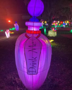 an illuminated bottle in the middle of a field at night with people walking around it