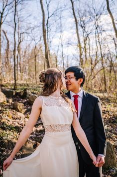 a bride and groom hold hands as they walk through the woods on their wedding day