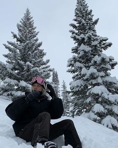 a woman sitting in the snow next to some trees