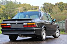 an old bmw is parked on the side of the road in front of some trees