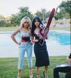 two women standing in front of a pool holding a chainsaw and a pink flamingo