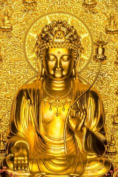 the golden buddha statue is sitting in front of a gold wall with candles on it