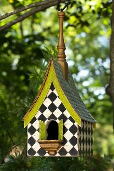 a birdhouse hanging from a tree branch in the woods with green and white checkered roof