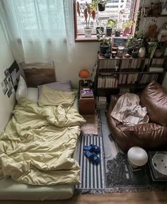 an unmade bed sitting next to a window in a room with lots of books