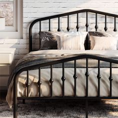 a black metal bed frame with pillows and blankets on it in front of a white brick wall