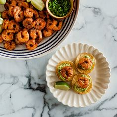 two plates filled with food on top of a marble counter next to a bowl full of shrimp