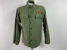 "Vintage 1950s U.S. Army military issue shirt. Made of green cotton. Has two chest pockets, a button down front and patches. About a size medium. Actual measurements are: 44\" at the chest 42\" at the waist 19\" shoulder seam to shoulder seam 23.5\" shoulder seam to cuff 28\" overall length In good condition with large paint stain on right cuff and a couple of small holes on sleeve and spots on back, see pictures." Olive Military Style Button-up Top, Green Military Style Button-up Shirt, Green Military Button-up Top, 1950s Shirts, Army Shirt, Military Patches, Military Shirt, Army Shirts, Military Patch