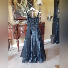 This Beautiful Black Dress Makes A Statement With Classic Style! It Features A 100% Acetate Fabric With A Beautiful Sheen, A Brocade Fabric Bust With Boning In Bodice, And Rosette Details Across Neckline. It's Lined With An Already Attached Crinoline Skirt To Provide Body To The Skirt And Has A Hidden Zipper. The Dress Is One Piece, But The Bodice Is Not Connected To The Skirt On The Outside To Give The Appearance Of A Separate Corset Style Top. Offers Welcome Armpit-To-Armpit: ~16" Waist: ~13.5" Top-To-Bottom: ~56" Wedding Dress, Goth, Photoshoot, Prom Dress, Homecoming Dress, Special Event Dress, Special Occasion Dress, Punk, Grunge Juniors 3/4, Women's Size 2 Black Satin Evening Dress With Fitted Bodice, Black Satin Maxi Dress With Fitted Bodice, Black Silk A-line Maxi Dress, Black Maxi Dress With Fitted Bodice For Formal Occasions, Sleeveless Black Silk Maxi Dress, Black Sleeveless Silk Maxi Dress, Black Silk Evening Dress For Formal Occasions, Black A-line Silk Maxi Dress, Black Silk Maxi Length Evening Dress