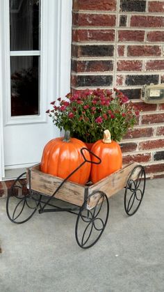 two pumpkins are sitting in a wooden wagon on the front porch with red flowers