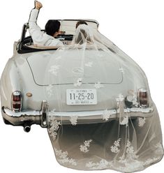 a bride and groom are in the back of an old car covered with a veil