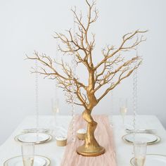 a gold tree centerpiece on a white table with plates and silverware in the foreground