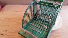 a green birdcage sitting on top of a wooden table