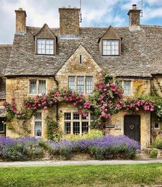 an old stone house with flowers growing on it's roof and windows in the front