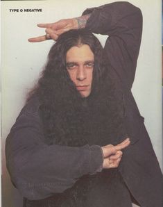 a man with long black hair holding his hands on his head and pointing to the side