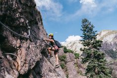 a man climbing up the side of a mountain with a rope attached to his back