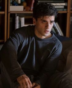 a young man sitting on top of a couch next to a book shelf