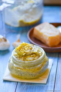 a glass jar filled with food sitting on top of a wooden table next to bread