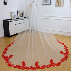 a white veil with red flowers on the floor in front of some pictures and frames