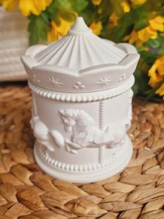 a white ceramic container with a horse on it sitting on a table next to yellow flowers